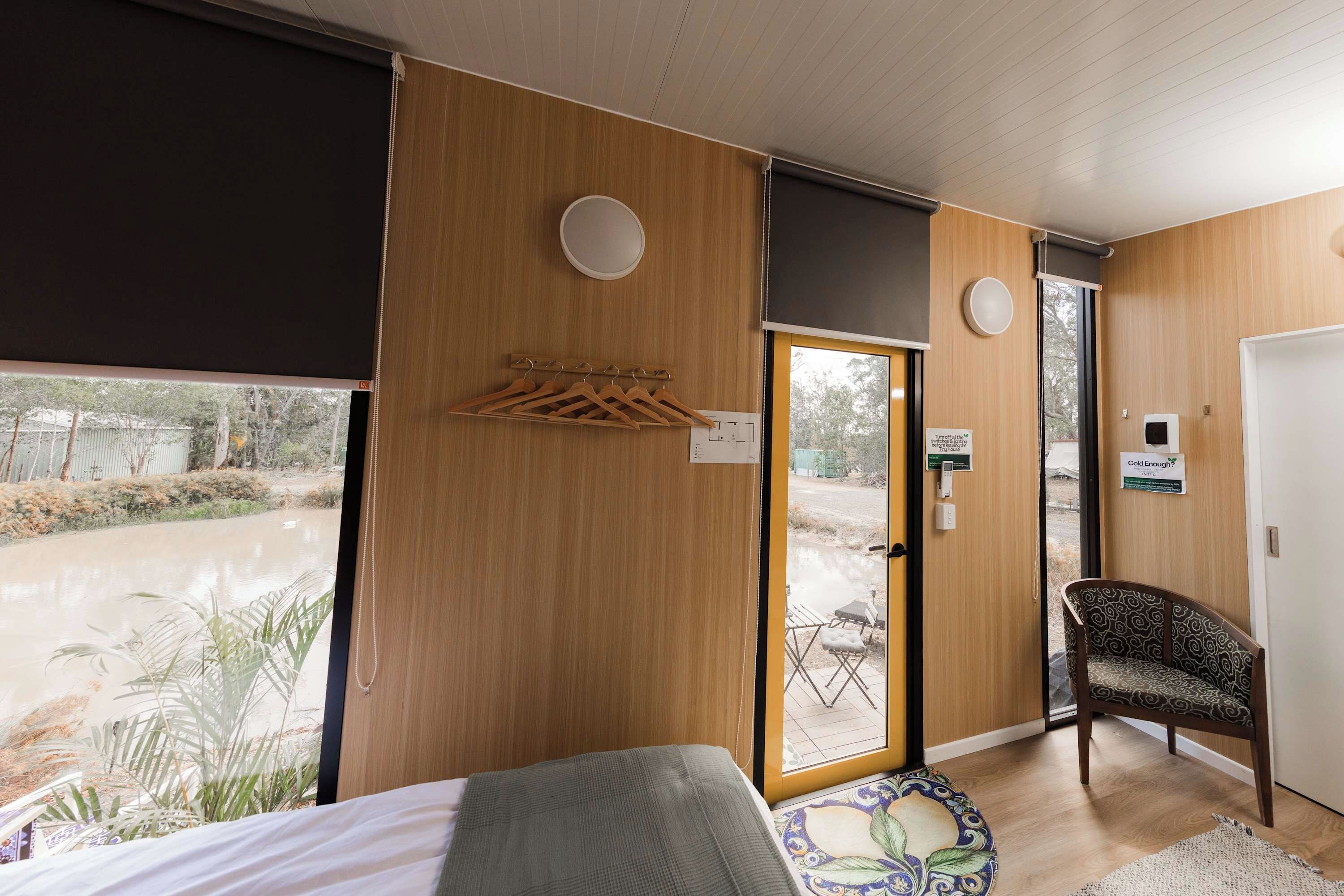 A hotel room with a bed, a chair, a small table, a window with a view of the outdoors, and a door with a sign.