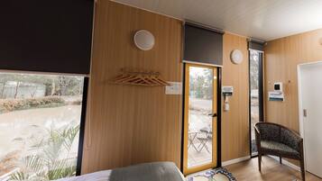 A hotel room with a bed, a chair, a small table, a window with a view of the outdoors, and a door with a sign.