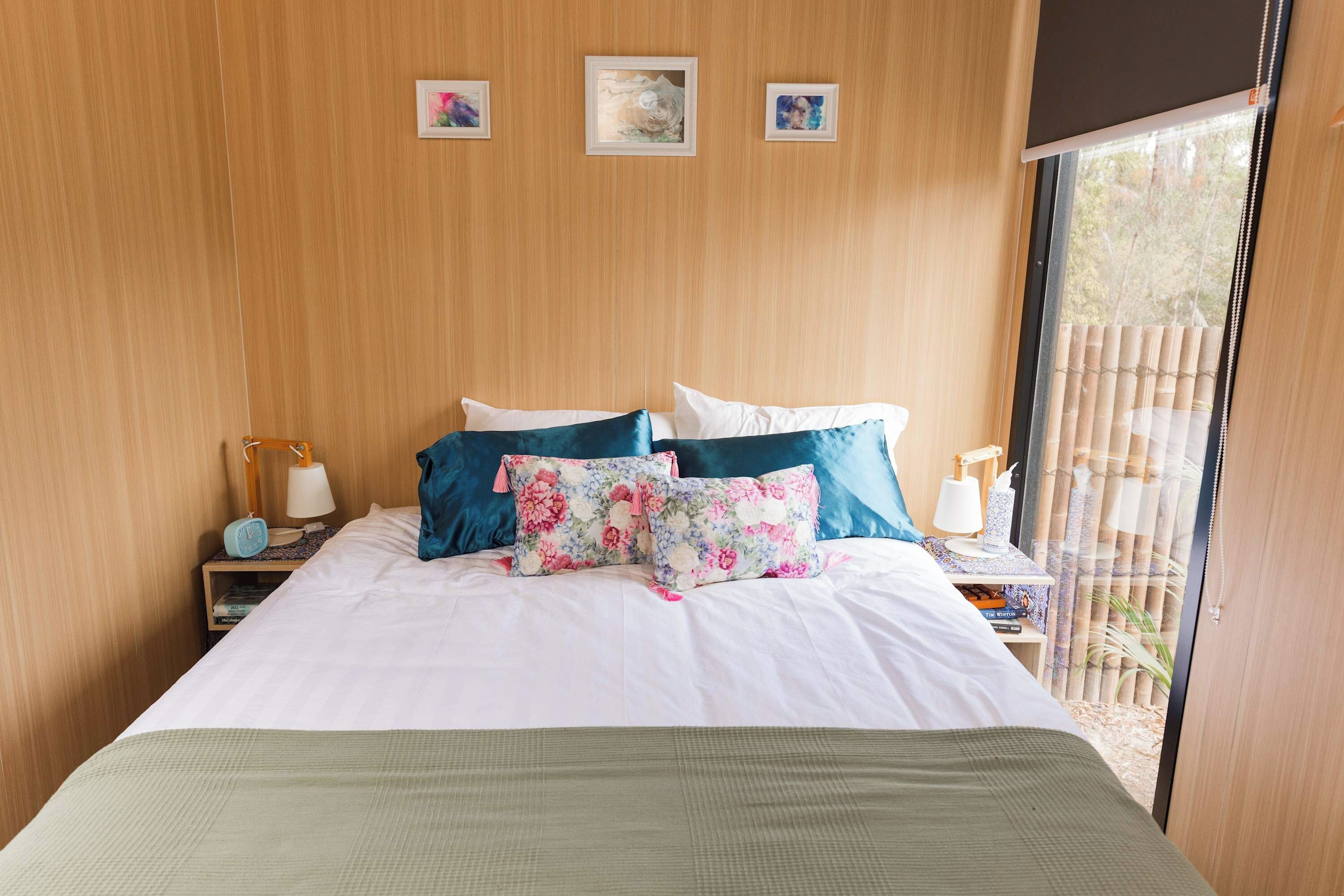 A bedroom with a bed, pillows, a nightstand, a lamp, and a window with a view.