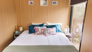 A bedroom with a bed, pillows, a nightstand, a lamp, and a window with a view.