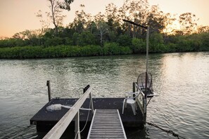 A wooden dock extending into calm water with a chair and a fishing net on it.