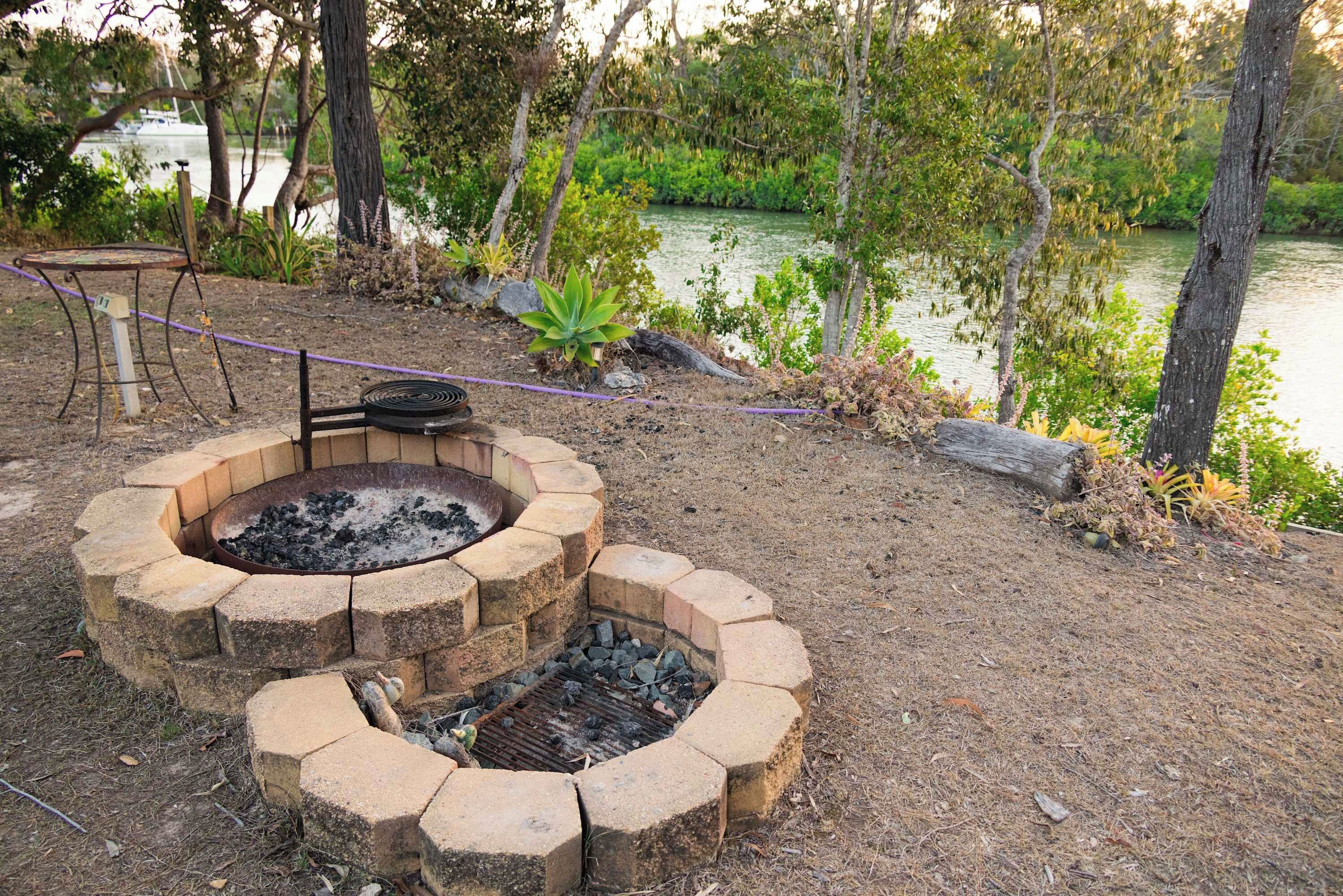 A fire pit area with a circular stone design, surrounded by dry grass and trees.