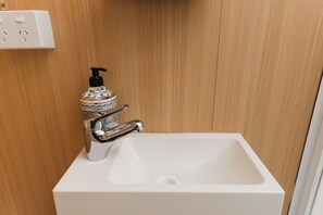 Une salle de bain avec un lavabo blanc, un robinet chromé et un distributeur de savon fixé au mur.