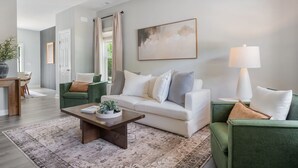 A living room with a sofa, coffee table, and a lamp. There is a door and a window in the background.