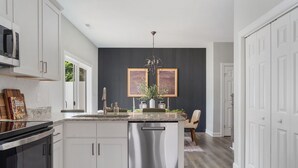 A modern kitchen with white cabinets, a stainless steel dishwasher, and a central island with a sink and countertop.
