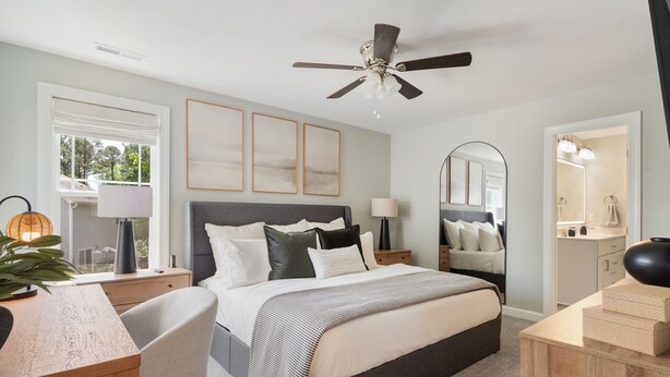 A bedroom with a bed, bedside tables, a desk, a chair, a ceiling fan, and a large mirror.