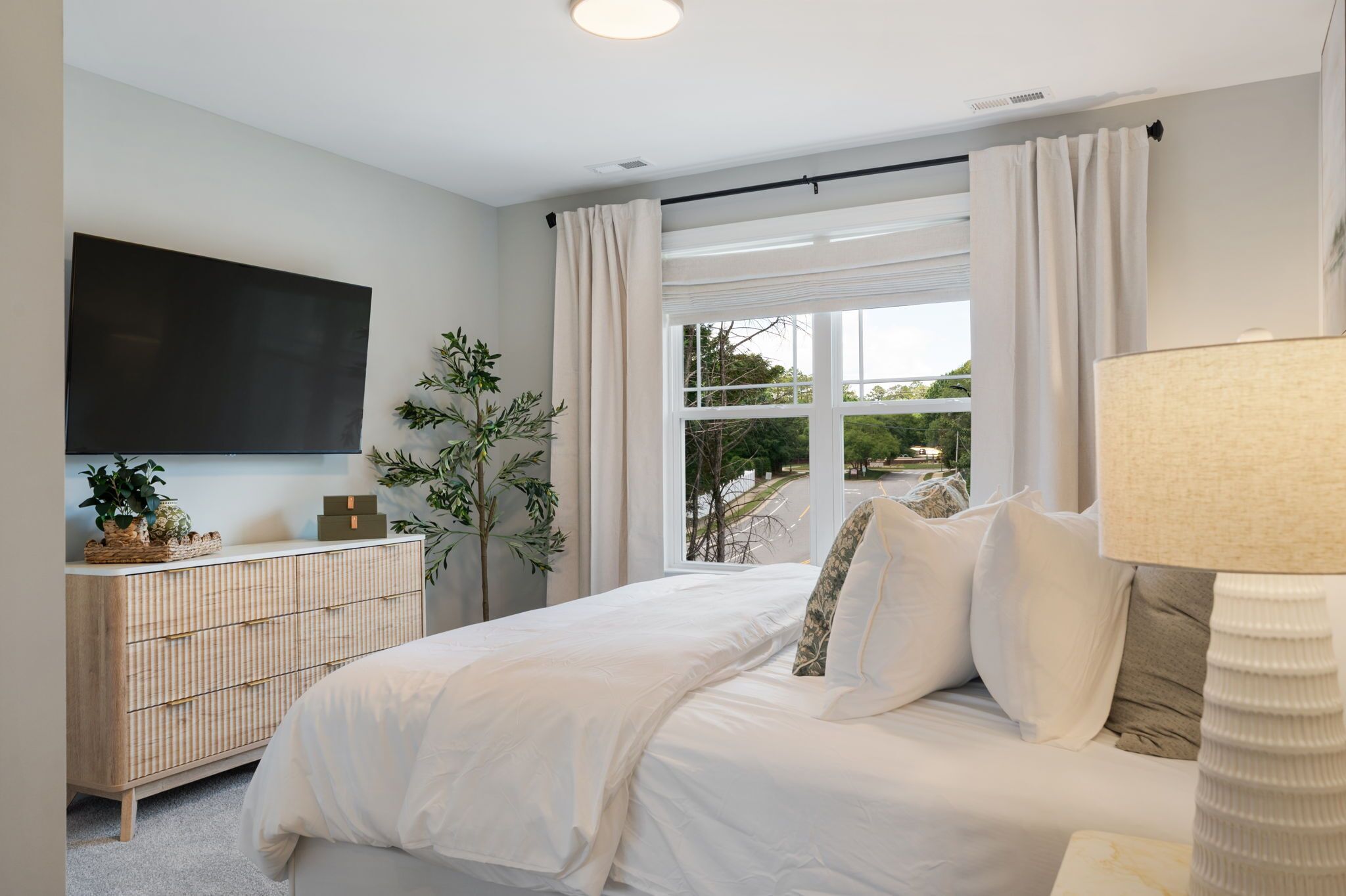 A bedroom with a bed, a TV, a dresser, and a window with curtains.