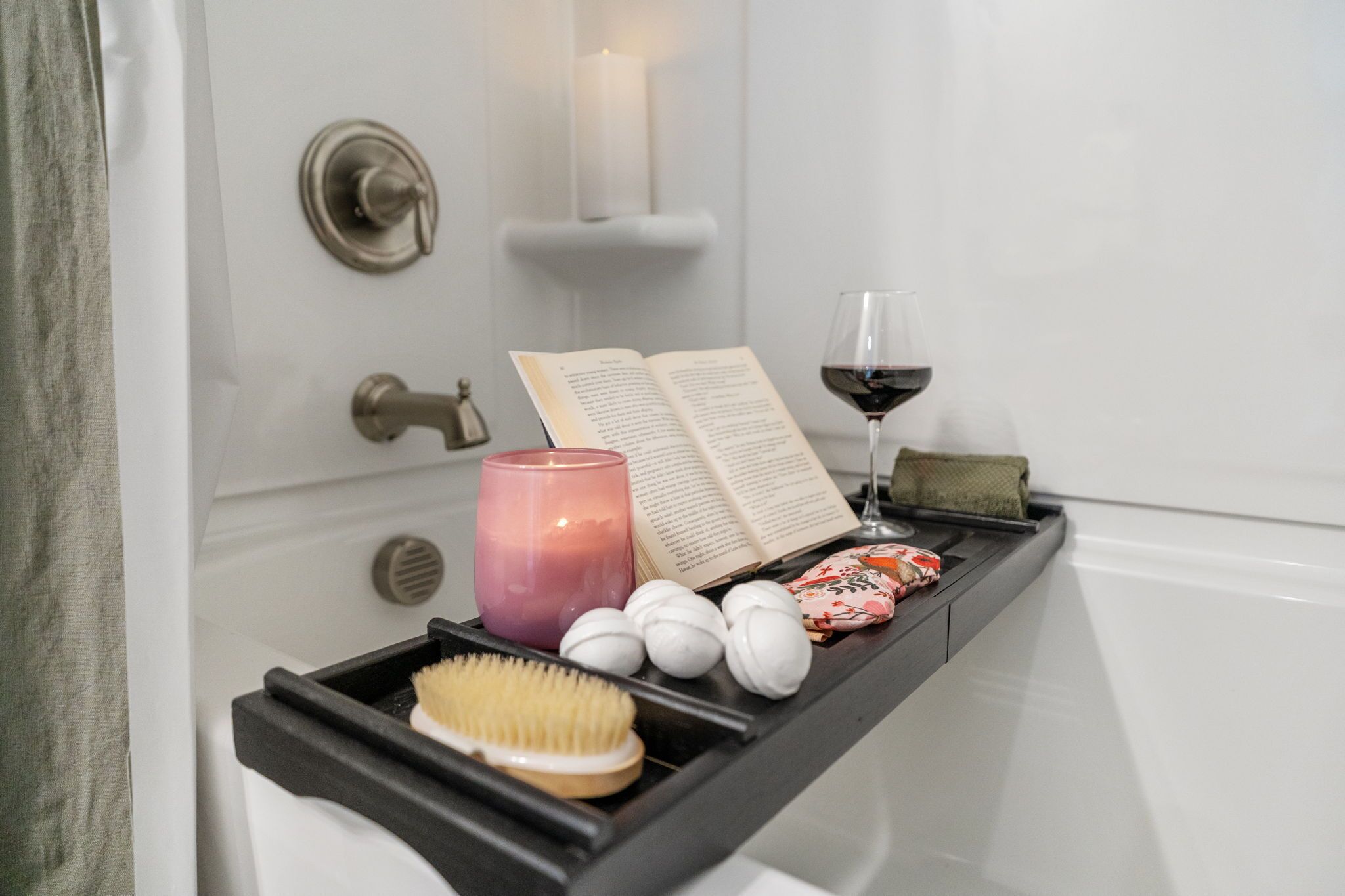 A bathroom vanity with a book, candle, and glass of wine.