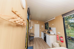 Eine kompakte Küche mit Mikrowelle, Toaster und Kaffeemaschine, ein kleiner Essbereich mit einem Stuhl und Holz-Wandhalterungen.