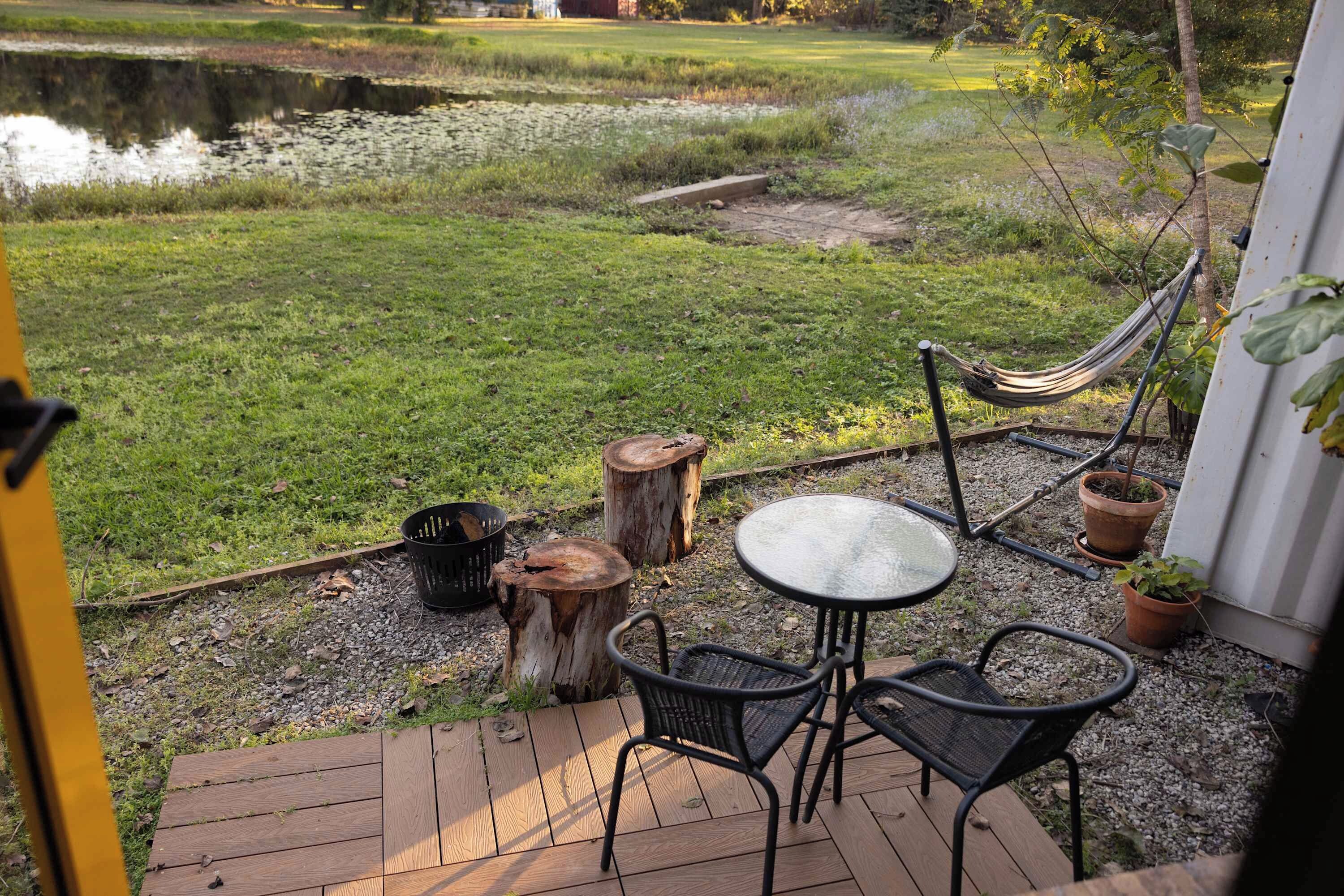 A deck with a table and chairs, a hammock, and a view of a pond and grassy area.