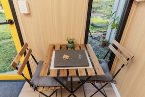 Une petite table en bois, sur laquelle se trouvent un ordinateur portable et une plante, accompagnée de deux chaises en bois dotées de coussins gris.