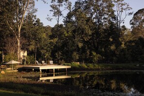 A lakeside deck with a table and chairs, surrounded by trees and a calm body of water. - Samford Valley Retreat by Tiny Away (Samford Valley)