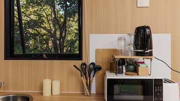A kitchen with a microwave, toaster, and coffee maker on a wooden countertop, a window with a view of trees, and a sink.