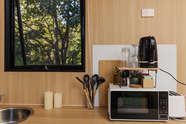 A kitchen with a microwave, toaster, and coffee maker on a wooden countertop, a window with a view of trees, and a sink.