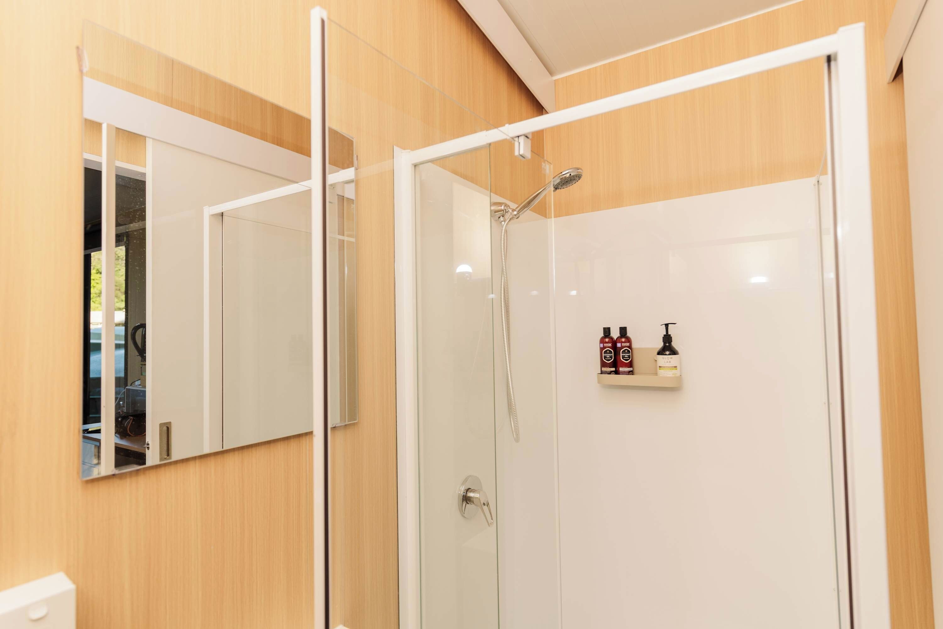 A modern bathroom with a glass shower enclosure, a mirror, and a shelf with toiletries.