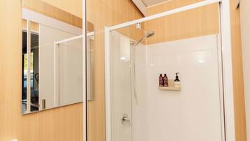 A modern bathroom with a glass shower enclosure, a mirror, and a shelf with toiletries.