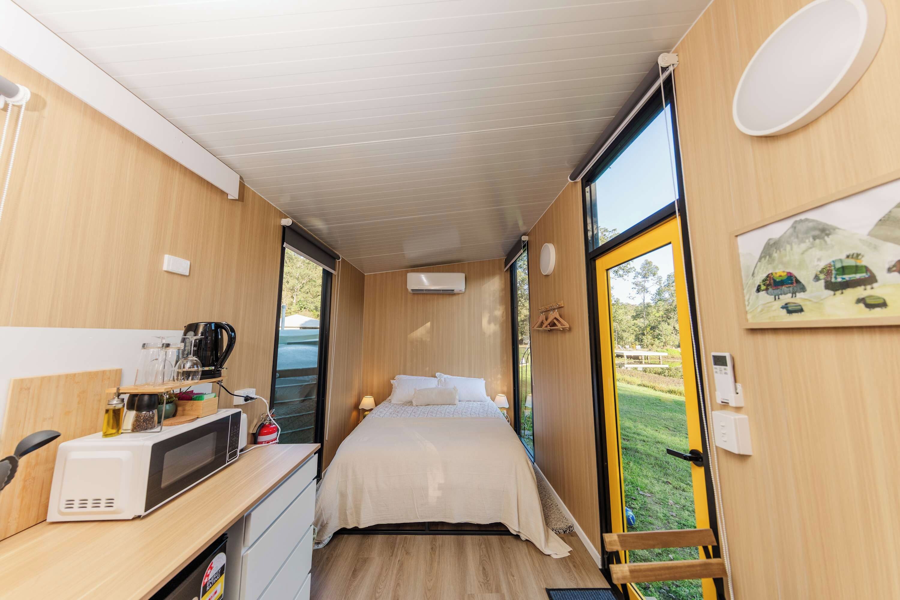 Habitación compacta con cama, una kitchenette pequeña, una ventana con vista a la vegetación y una puerta que da al exterior.