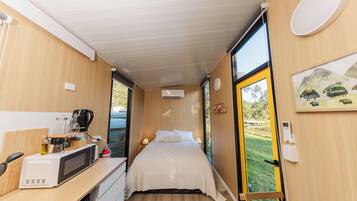Habitación compacta con cama, una kitchenette pequeña, una ventana con vista a la vegetación y una puerta que da al exterior.
