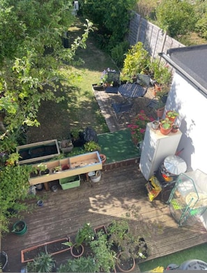 A wooden deck with potted plants, a small garden area, and a white wall. - Modern 2BR London Retreat With Garden Parking (London)