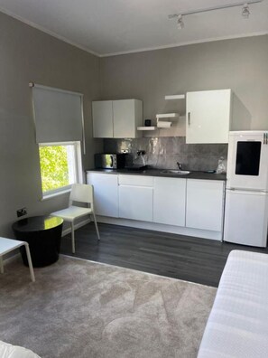 A modern kitchen with white cabinets, a black countertop, and a refrigerator. There is a window with a view of greenery outside. - Stylish Private Room in Croydon With Free Street Parking (London)