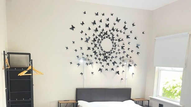 A bedroom with a bed, a dresser, a desk, and a wall with butterfly decals. - Bright Double Room in Croydon Free Street Parking (London)