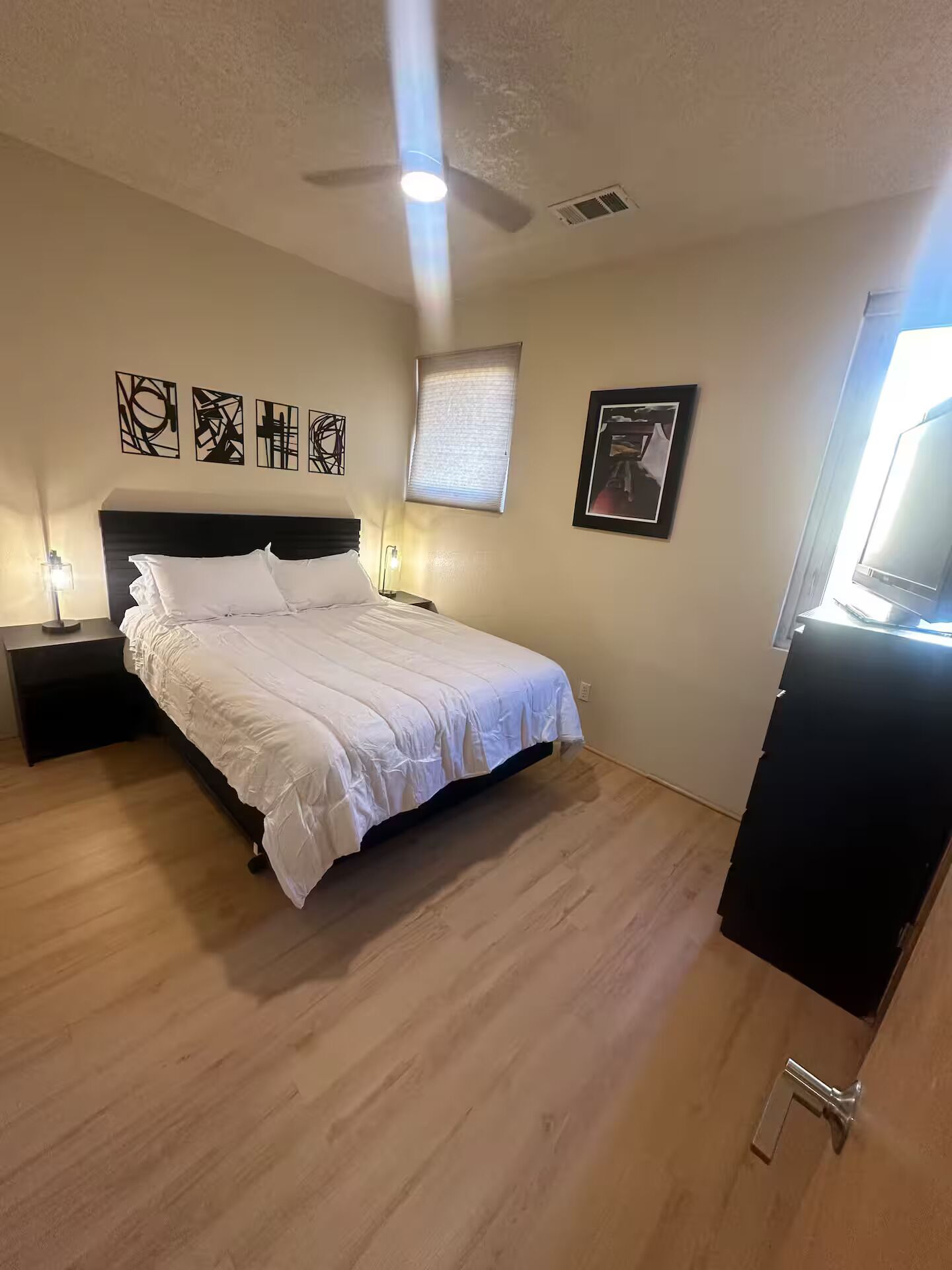 Une chambre à coucher comprenant un lit, des tables de chevet, un ventilateur de plafond, des œuvres d’art et un téléviseur.
