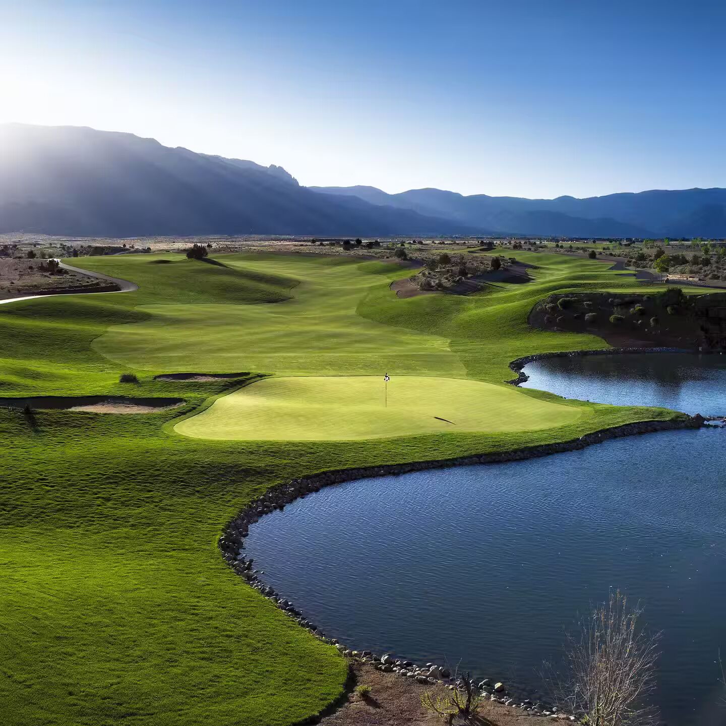 A golf course with a water body and mountains in the background.