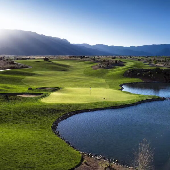 A golf course with a water body and mountains in the background.