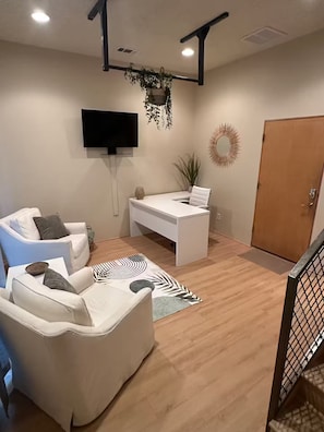 A modern living room with a white sofa, a white desk, and a television mounted on the wall. - Silver Lofts (Albuquerque)
