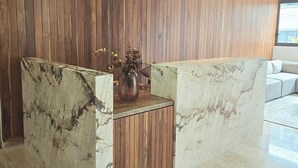 Uma área de recepção com painel de parede de madeira, balcão de mármore e luminária pendente.