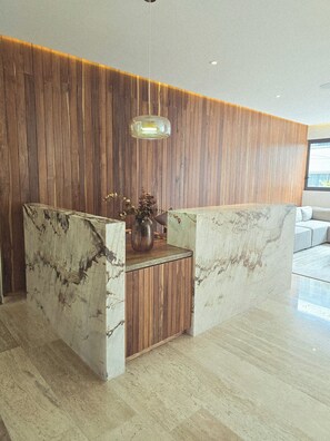 A reception area with a wooden panel wall, a marble reception desk, and a hanging light fixture. -  Playa Condo with  Rooftop pool & ocean view - walking  to famous 5ta & Beach. (Playa del Carmen)