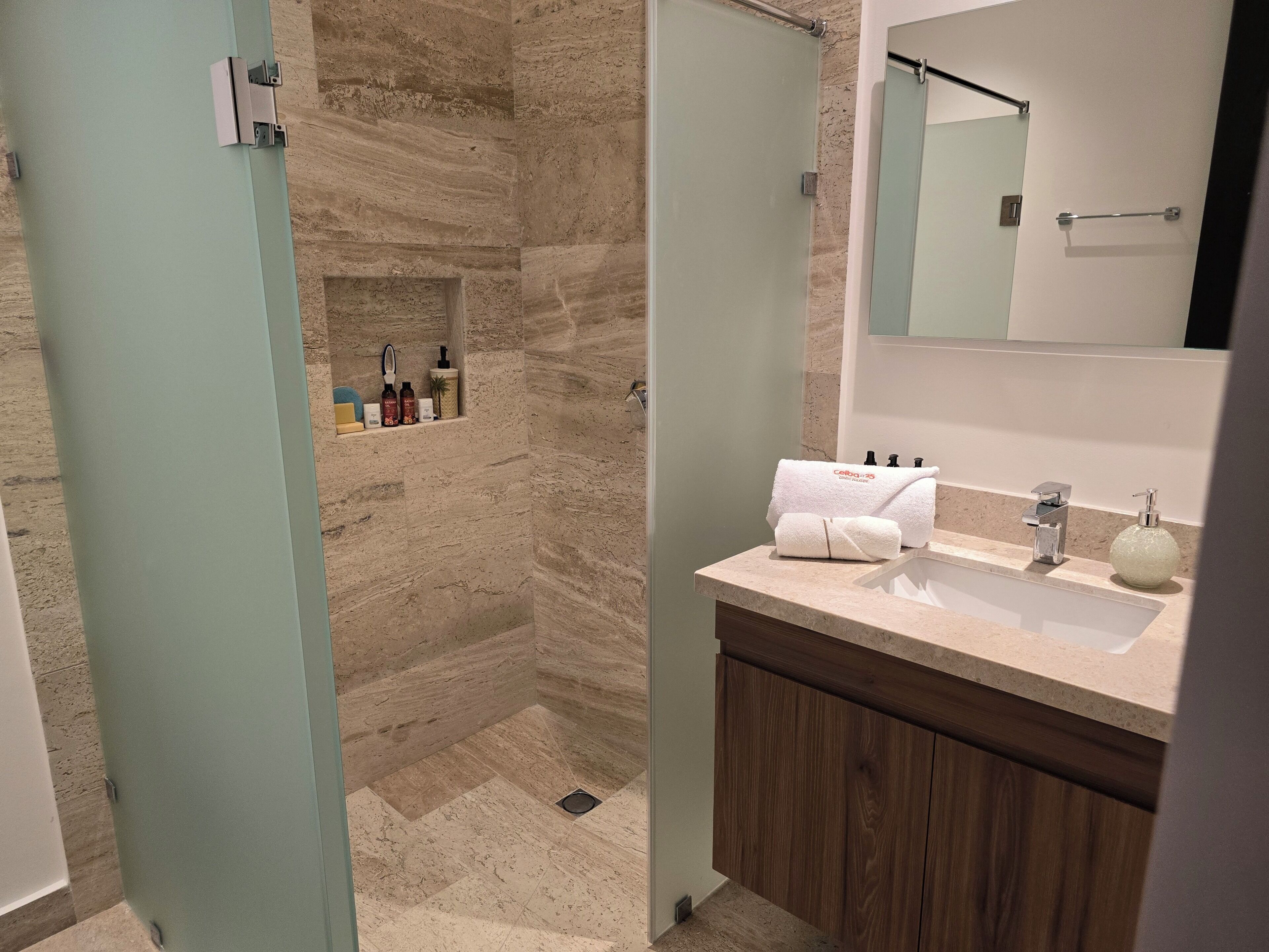 Un baño moderno con ducha, tocador con espejo y artículos de aseo.