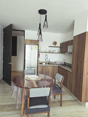 A modern kitchen with a central island, wooden cabinets, and a dining area with a round table and chairs. -  Playa Condo with  Rooftop pool & ocean view - walking  to famous 5ta & Beach. (Playa del Carmen)