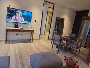 Ein modernes Wohnzimmer mit einem wandmontierten Flachbildfernseher, einem Holztisch, einem Esstisch mit Stühlen und einem kleinen Hocker.