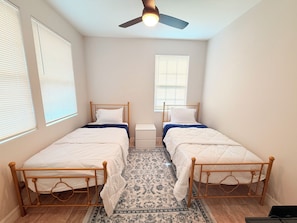 A bedroom with two single beds, a ceiling fan, and a patterned rug. - Nice 2-bedroom house with AC in welcoming Houston neighborhood (Houston)