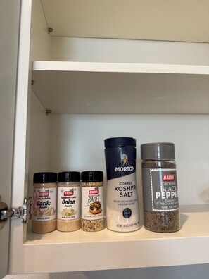 Ein Regal mit verschiedenen Gewürzbehältern, darunter Knoblauchpulver, Zwiebelpulver, Bagel-Gewürz, koscheres Salz und schwarzer Pfeffer.