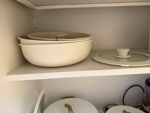 Ein Küchenregal mit weißen Keramiktöpfen und Deckeln.