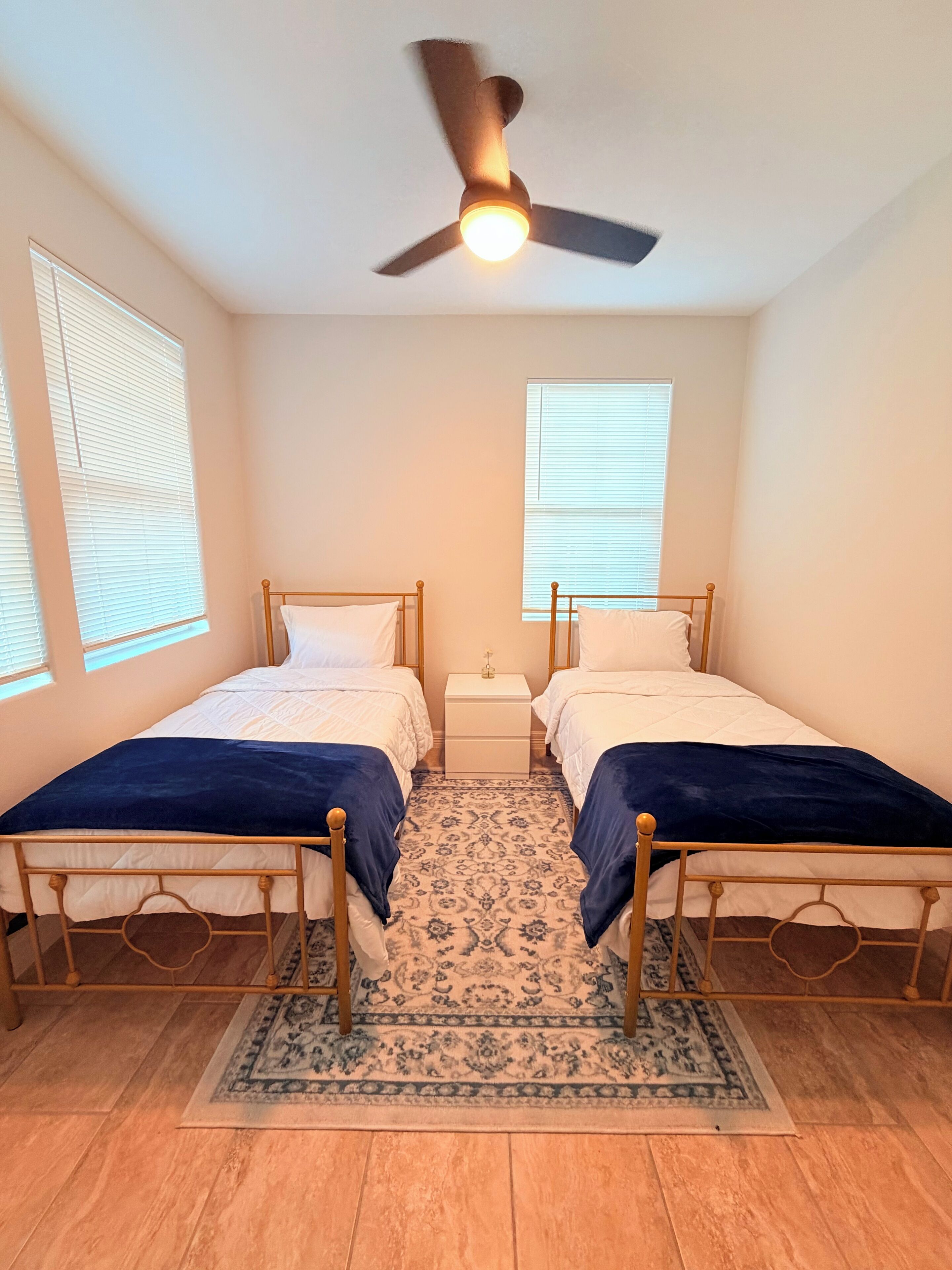 Ein Schlafzimmer mit zwei Einzelbetten, einem Deckenventilator und einem gemusterten Teppich.