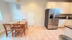 A kitchen with a stainless steel refrigerator, white cabinets, a dining table with chairs, and a tiled floor.