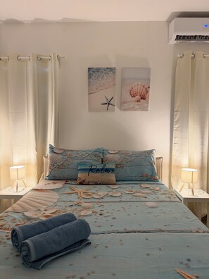 A bedroom with a bed, two wall-mounted air conditioners, a window with curtains, and a wall with two framed pictures. - The Best Location in Bayahibe (Bayahíbe)