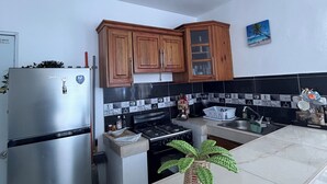 Een keuken met een roestvrijstalen koelkast, houten kastjes, een gasfornuis en een hangende lamp.