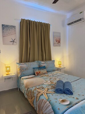 A bedroom with a bed, two bedside lamps, a wall-mounted air conditioner, and a curtain.