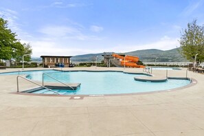 Ein Schwimmbecken mit Rutsche, einem Rettungsschwimmerstand und Blick auf Hügel.