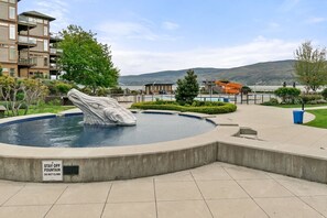 Ein Schwimmbecken mit einer Skulptur, einem Schild mit der Warnung vor Klettern sowie Blick auf Hügel und ein Gewässer.