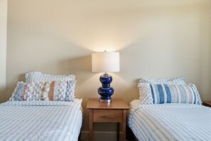Ein Hotelzimmer mit zwei Betten, einem Nachttisch mit Lampe und einer schlichten Wand.