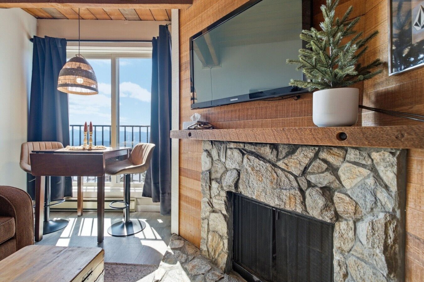 Een moderne woonkamer met een stenen openhaard, een televisie erboven en een eethoek met een tafel en stoelen.