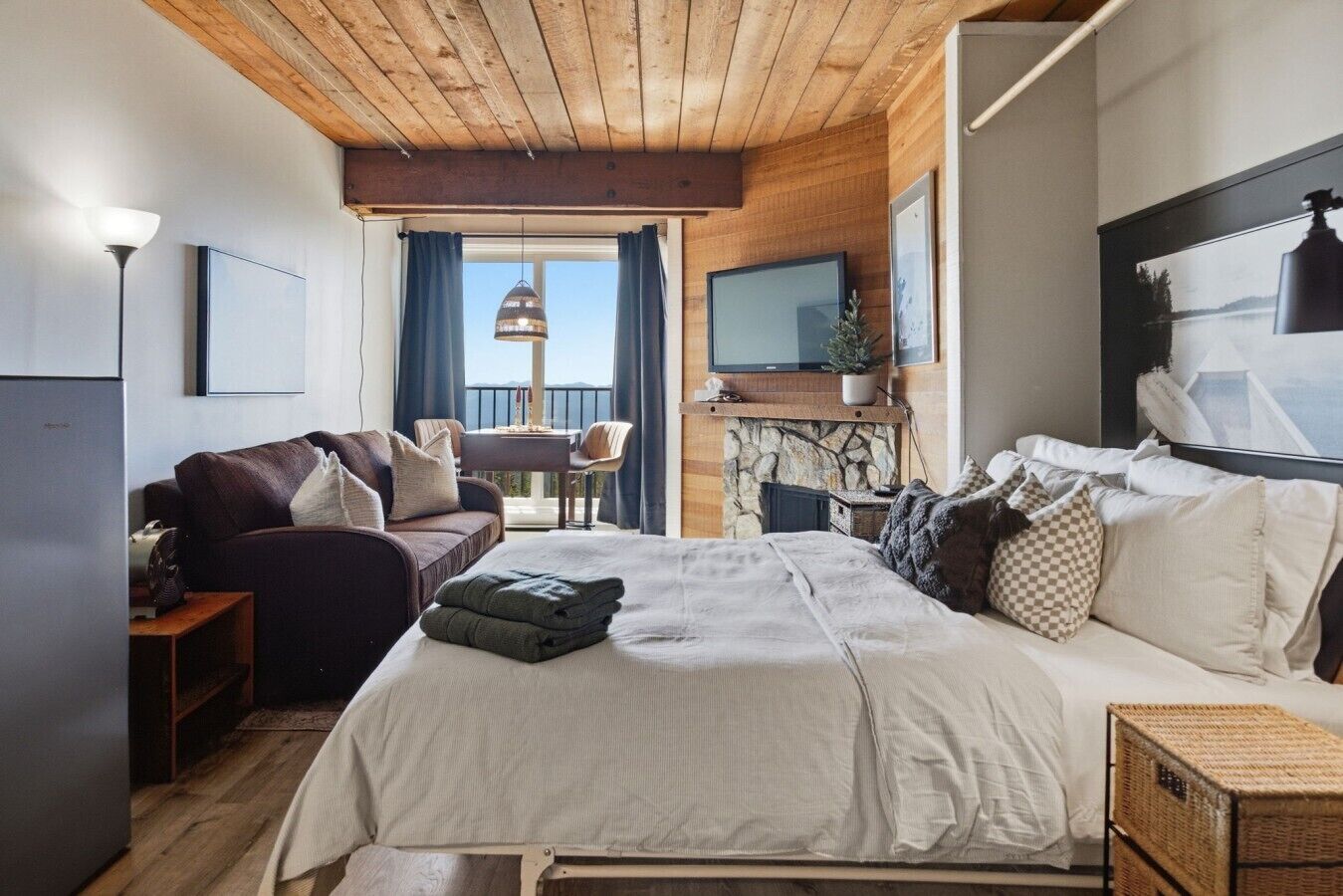 A bedroom with a bed, a sofa, a television, and a stone fireplace.