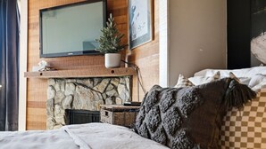 Et soveværelse med en stenvægges pejs, et tv ophængt over den, og en seng med pude i skakmønster.