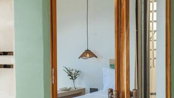 A bedroom with a bed, bedside table, lamp, and a view through a door.