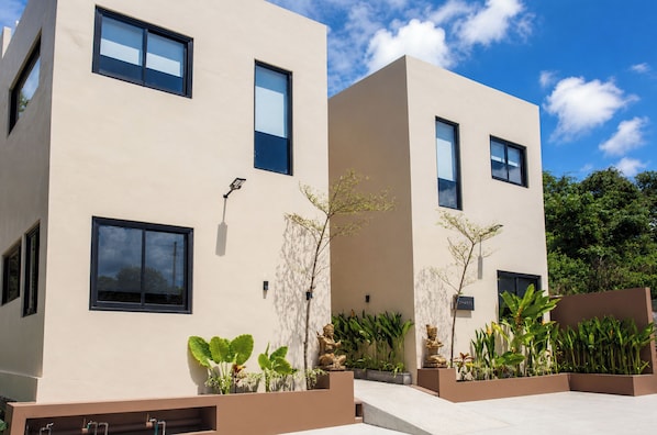 A modern building with multiple windows, a flat facade, and a well-maintained garden with various plants.